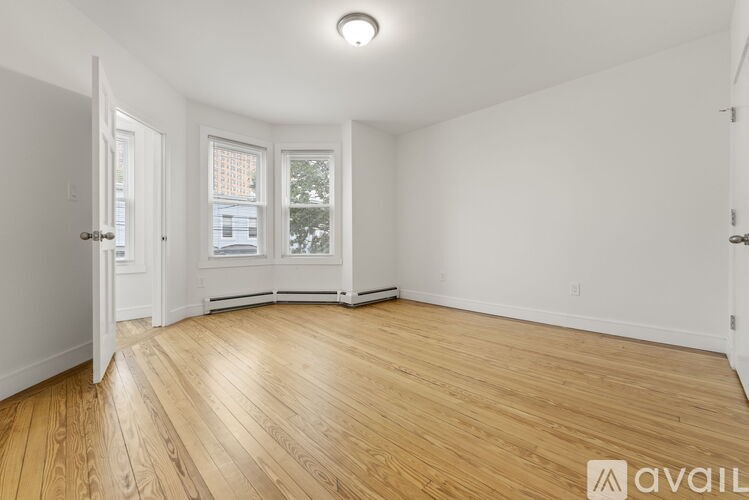 A room with wooden flooring and white walls, with a window showing a view of a building outside.