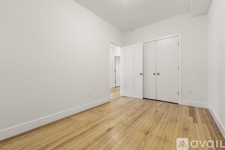 A room with wooden flooring and white walls, featuring a white door and a white wardrobe.