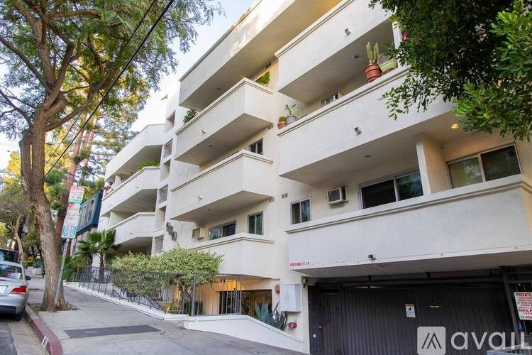 A white apartment building with balconies and a car parked on the street.