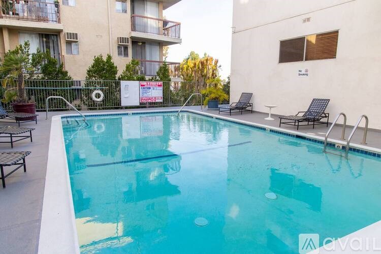 A pool with chairs around it and apartment buildings in the background.