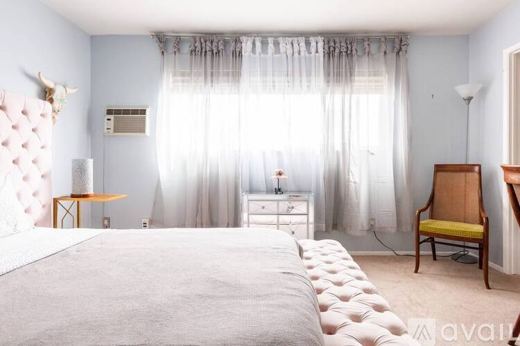 A bedroom with a large bed, a chair, and a dresser with a curtain.