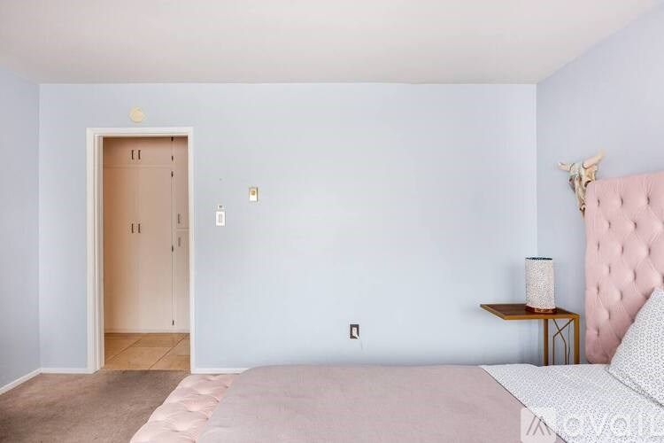A bedroom with a pink headboard bed and a small table with a lamp.