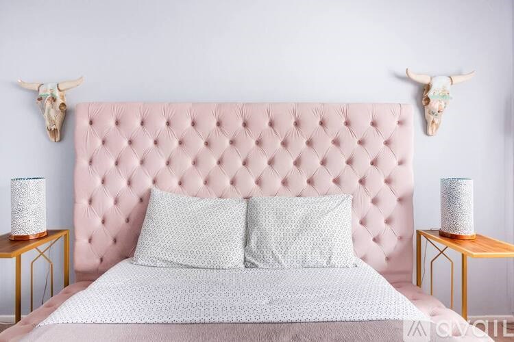 A bed with a pink headboard and two pillows is flanked by two small tables with lamps on them.