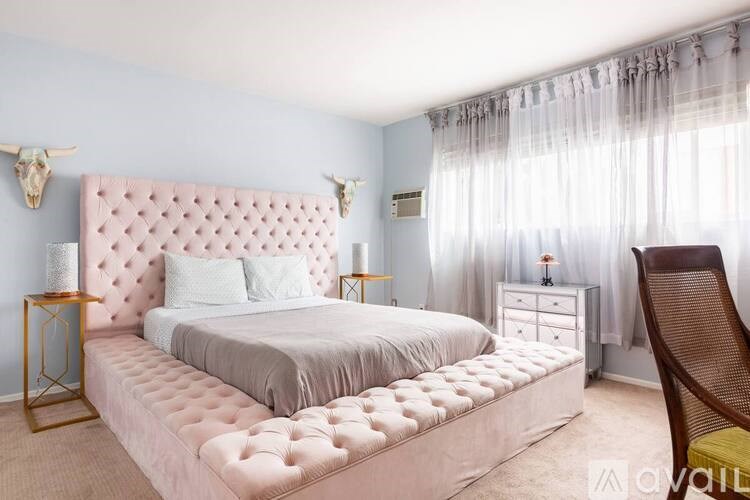 A bedroom with a pink tufted headboard and a white bedspread.