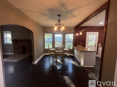 A dining room with a fireplace and a kitchen area in the background.