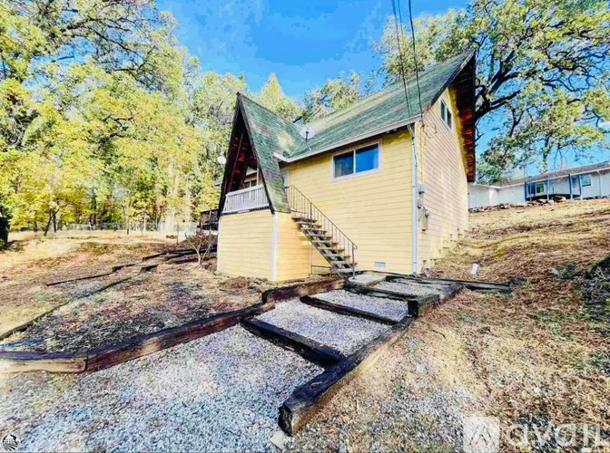A small yellow house with a green roof is surrounded by trees.