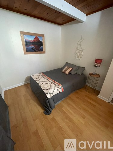 A bedroom with a bed, a painting on the wall, and a wooden floor.