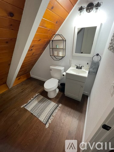 A small bathroom with wood flooring and a white toilet and sink.