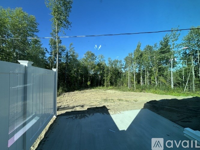 A clear blue sky above a forested area with a fence on the left side.