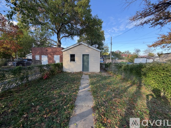 A small building with a grey roof is surrounded by a fence and trees.