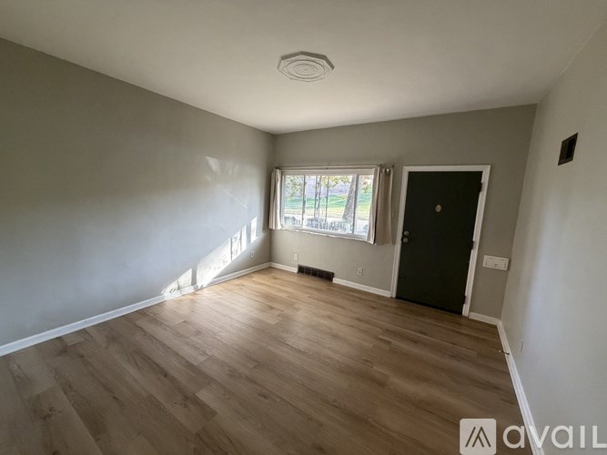 A room with wooden flooring and a window with white curtains.