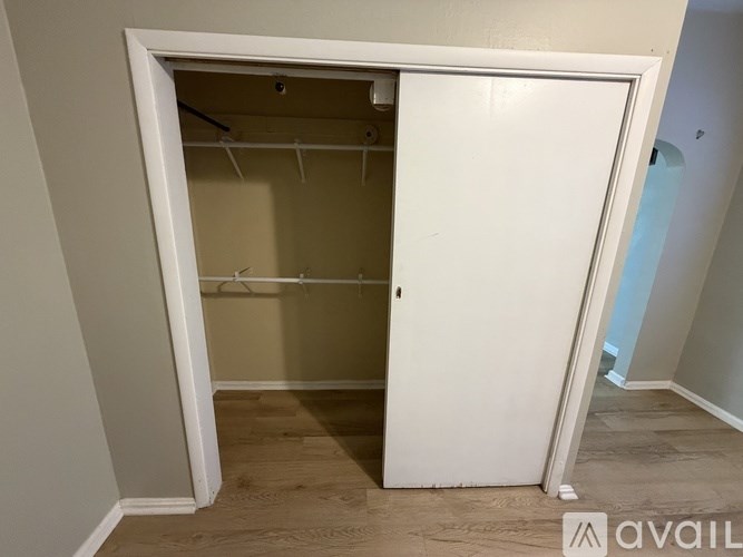 A white closet with a door open and clothes hanging inside.