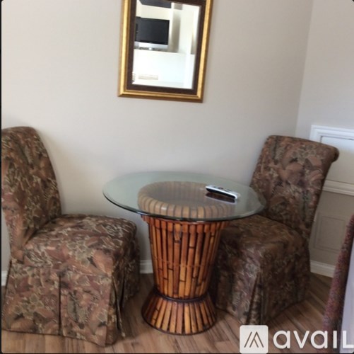 A glass table with a wicker base is surrounded by two chairs with matching patterned upholstery.