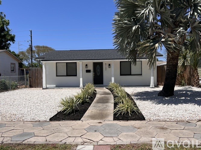 A white house with a black roof and a gravel driveway in front.