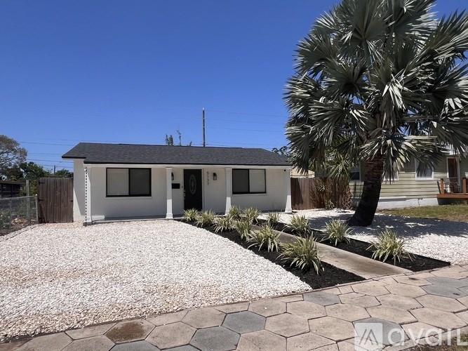 A small white house with a grey roof and a palm tree in front.