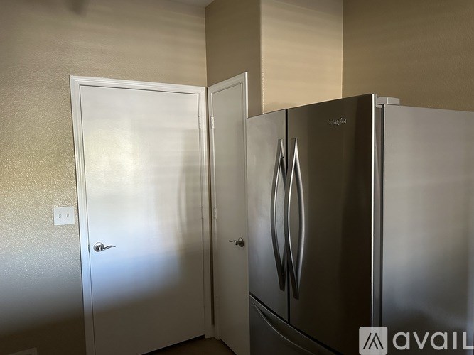 A stainless steel refrigerator with a door open is in a room with a white door.
