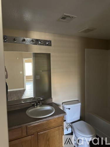 A bathroom with a toilet, sink, mirror, and a white bathtub.