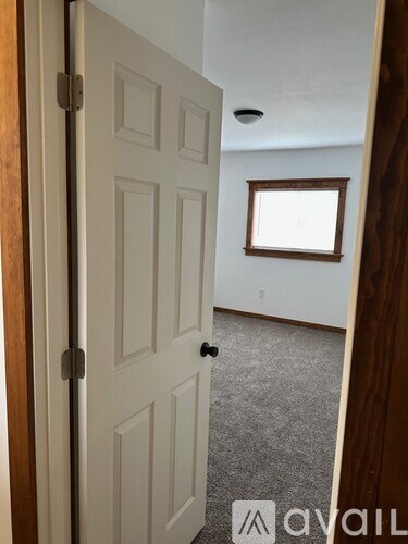 A white door with a black handle is open to a room with a window.