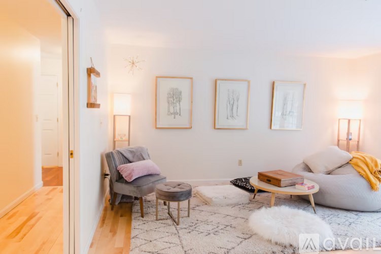 A living room with a grey couch, a grey armchair, a white rug, and three framed pictures on the wall.