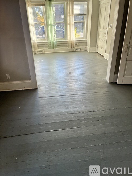 A room with wooden floors and a window with green curtains.