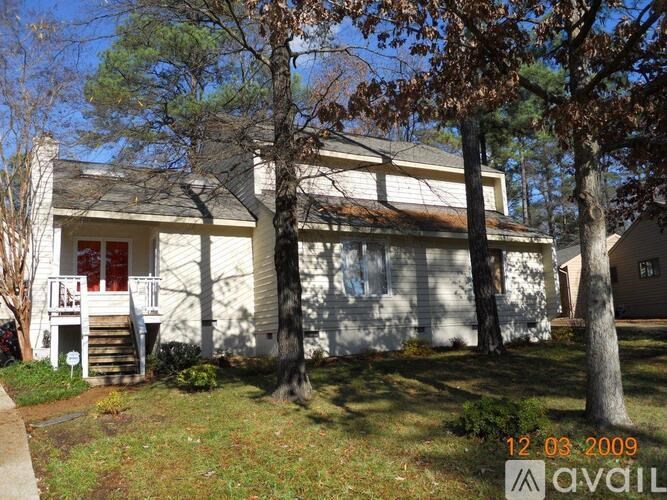 A white house with a porch and a tree in front of it.