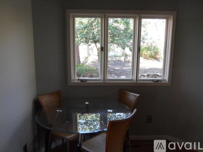 A glass table with four chairs is in front of a window.