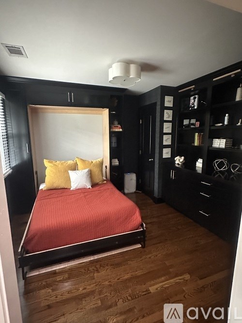 A bedroom with a red bedspread and a black bookshelf.