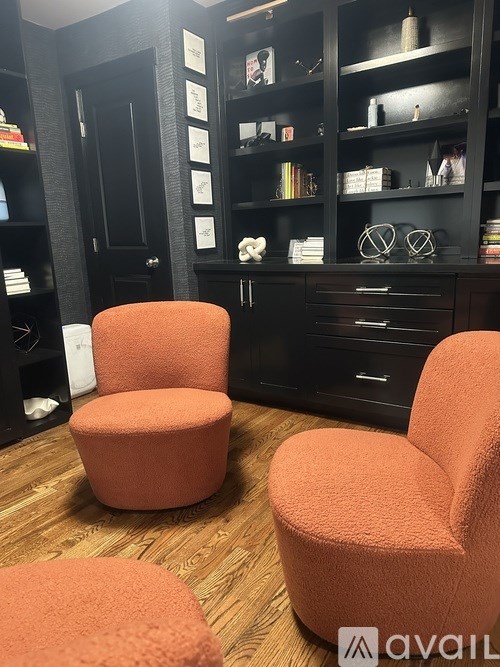 Two orange chairs in front of a black bookshelf.