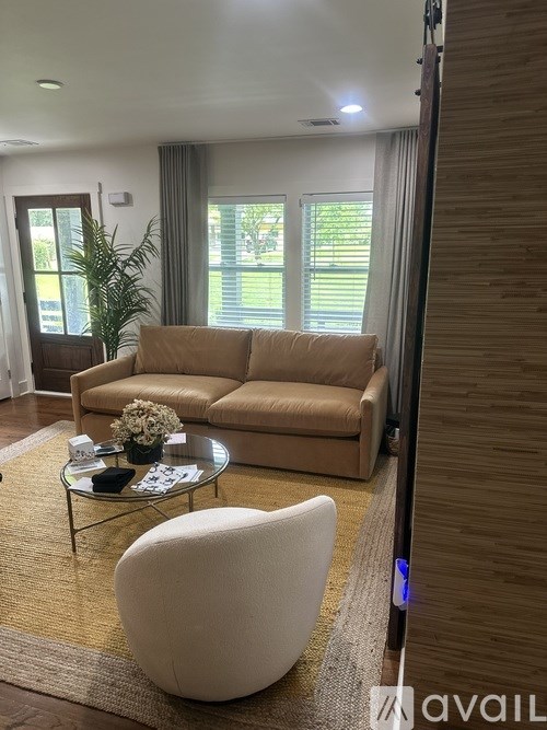 A living room with a beige couch, a glass coffee table, and a white chair.