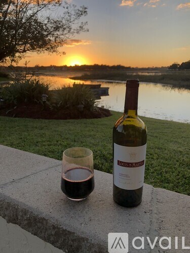 A bottle of wine and a glass of wine are on a ledge with a sunset in the background.
