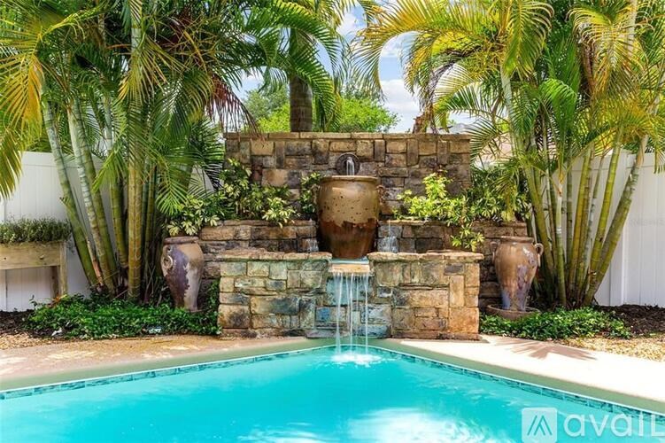 A pool surrounded by palm trees and a stone fountain.