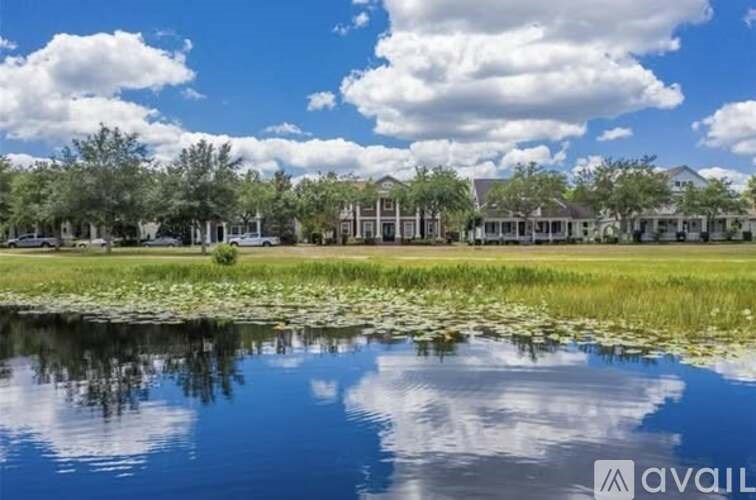 A serene landscape with a pond, lily pads, and a row of houses.