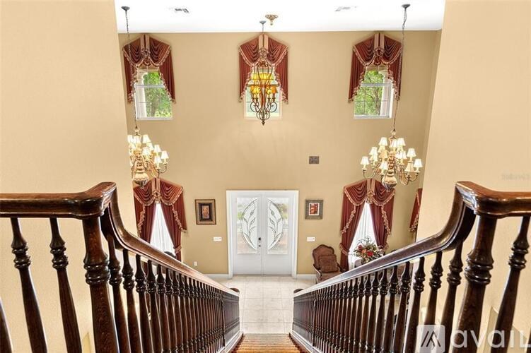 A grand staircase with a chandelier and two windows with red curtains.