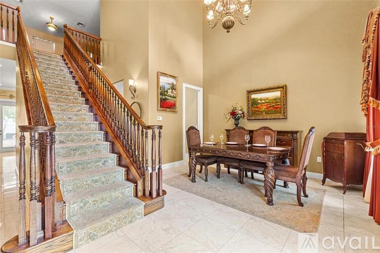 A wooden staircase with a carpeted floor and a chandelier hangs above a dining table with chairs.