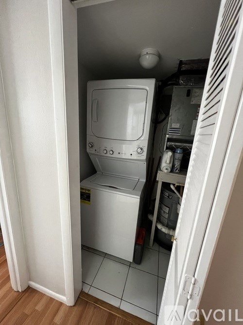 A small white washing machine is in a narrow space between a wall and a cabinet.