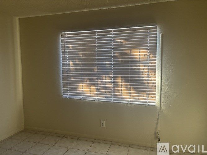A room with a window covered by blinds and a person sitting in front of it.