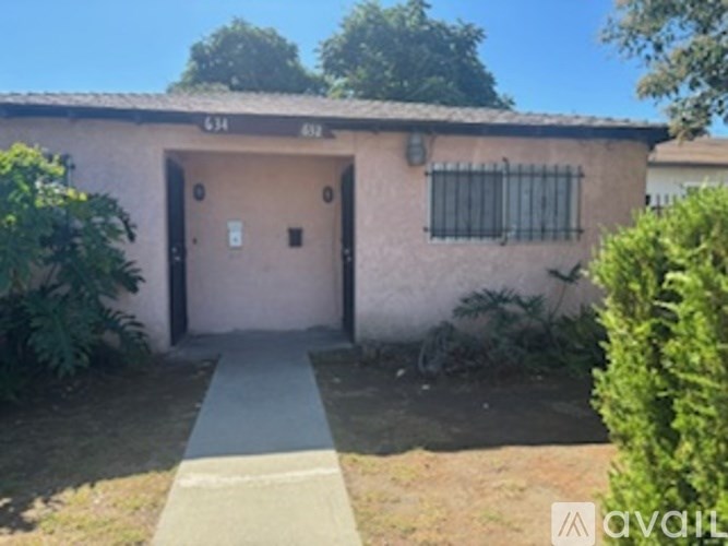 A small building with a door and a window is surrounded by greenery.