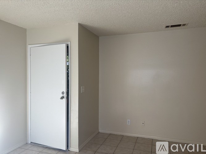 A white door is in a room with a tile floor and a wall socket.