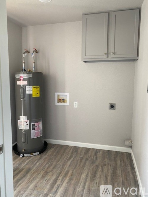 A room with a grey floor and a grey wall with a grey cabinet and a grey water heater.