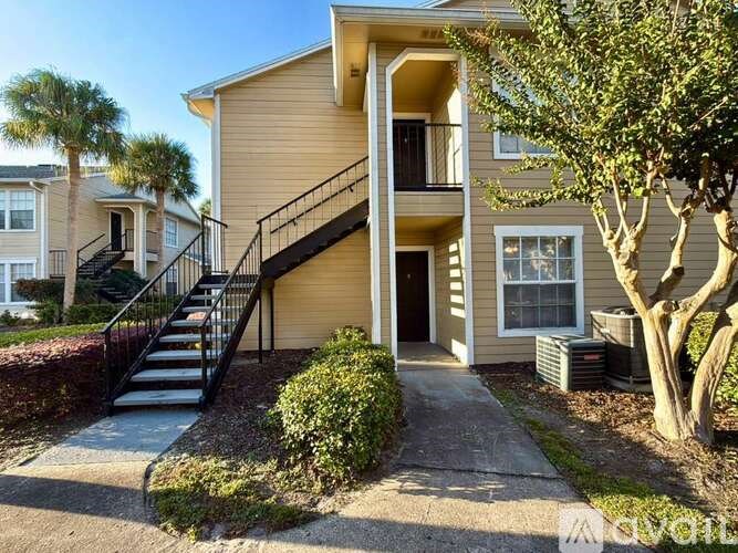 A beige two-story apartment building with a staircase leading to the entrance.