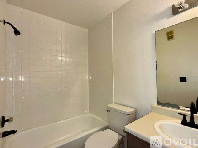 A white tiled bathroom with a toilet, sink, and bathtub.