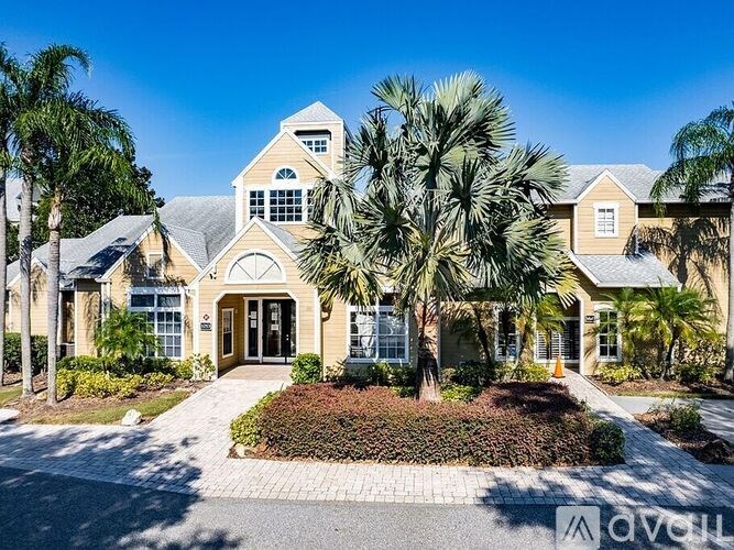 A large house with a driveway and palm trees in front.