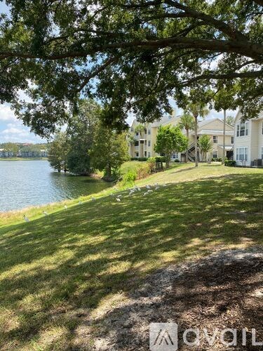 A grassy area with a tree in the foreground and apartment buildings in the background.