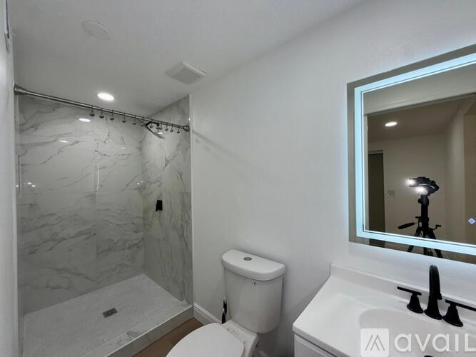A bathroom with a marble shower, toilet, and sink.
