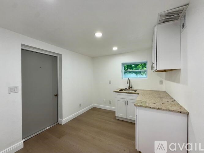 A kitchen area with a sink, cabinets, and a window.