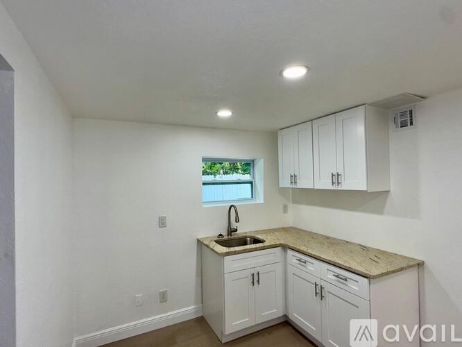 A kitchen with white cabinets and a window overlooking a pool.