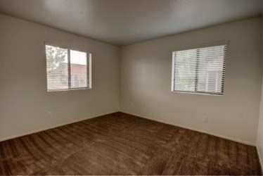 A room with brown flooring and two windows.