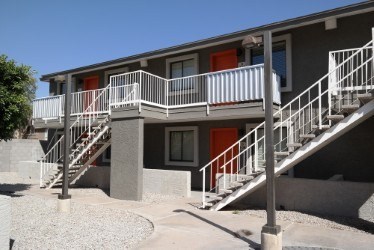 A concrete building with a red door and a white railing.