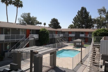 A pool is surrounded by a concrete fence and stairs leading to apartment buildings.