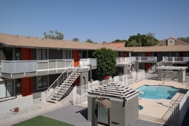 A pool is surrounded by a white fence and a building with red trim.